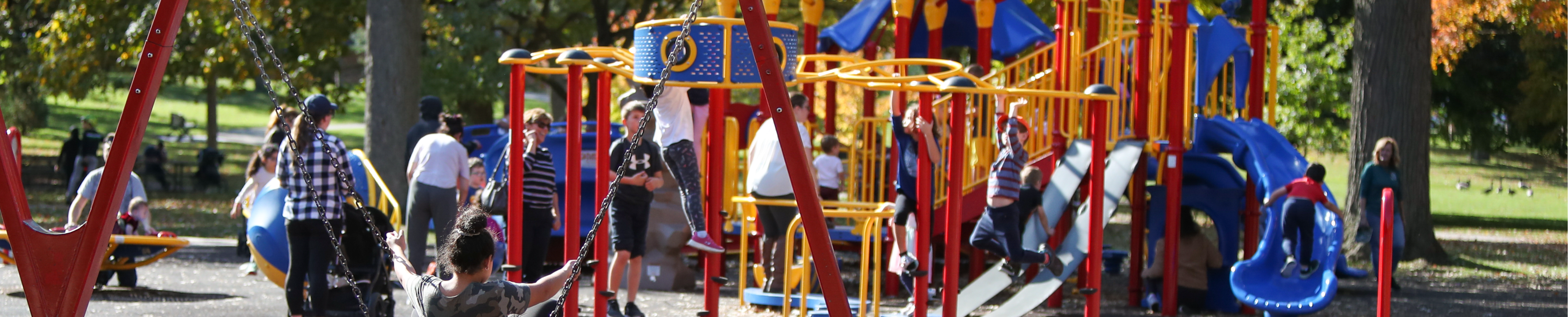 A paved path runs through Gibbons Park in London, Ontario, lined with orange trees, many orange leaves on the ground.