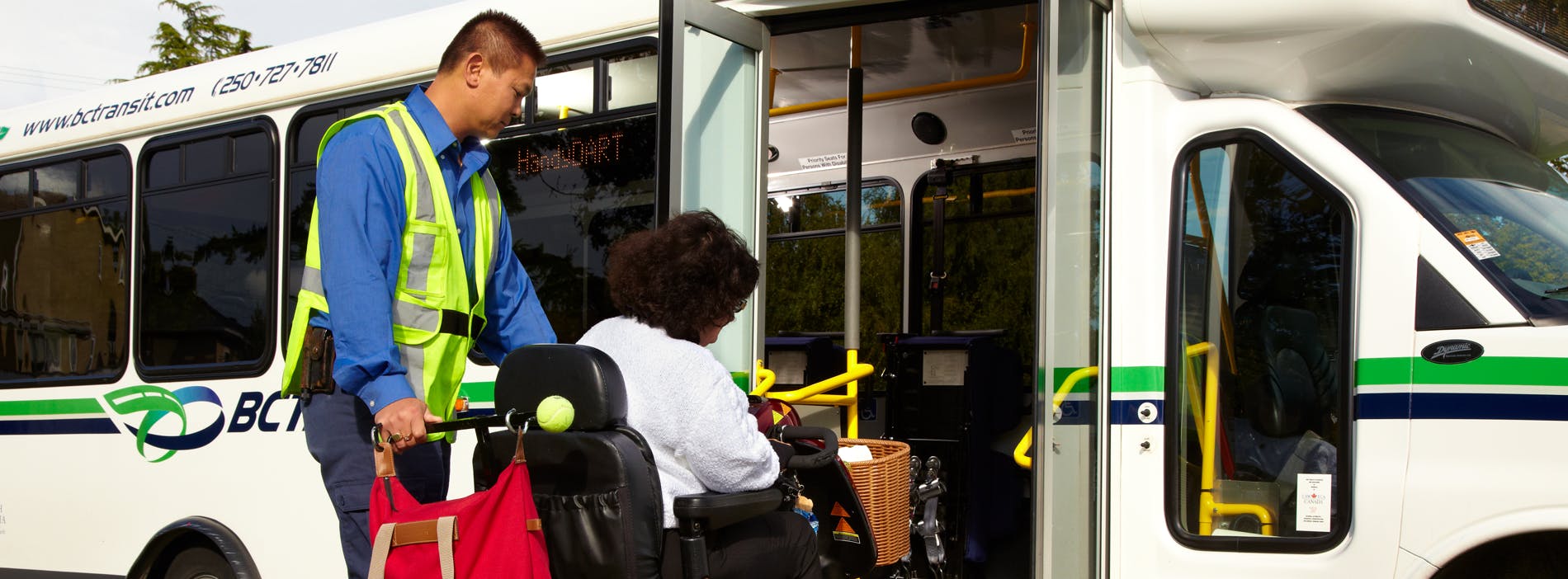 A picture of a handyDART drive supporting a rider in a power chair up the bus ramp