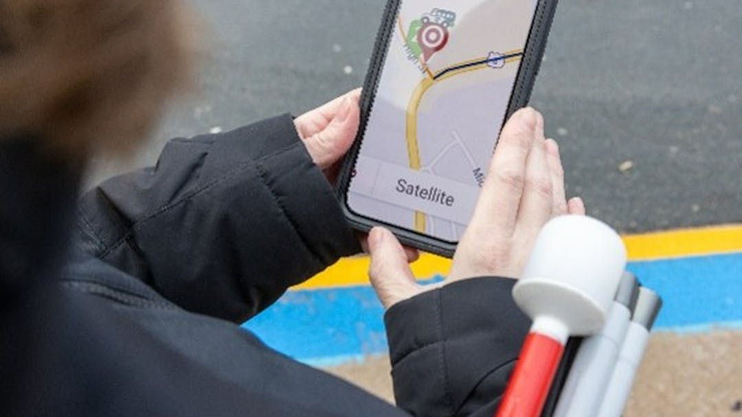 A person with a white cane looking at a digital map on their cellphone.