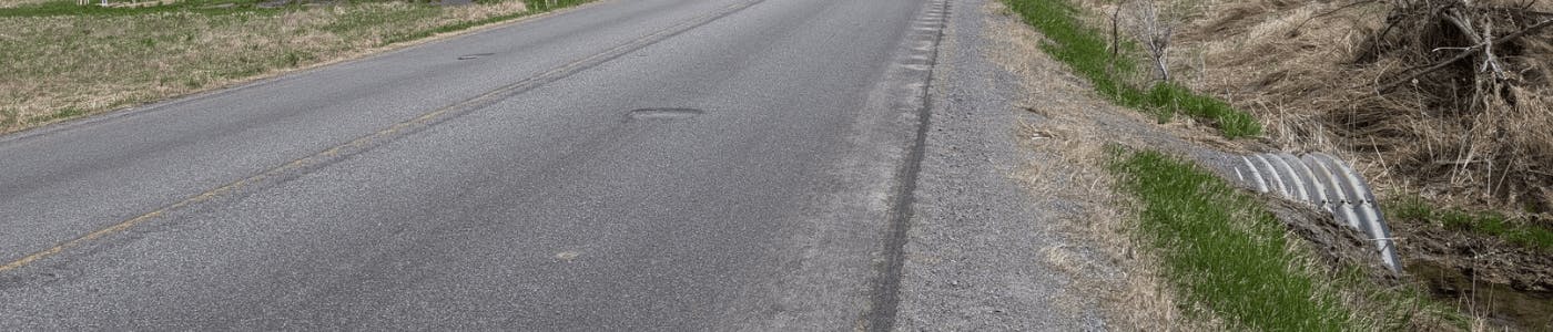 Photo of a road with a culvert coming out from under the right side of the road.