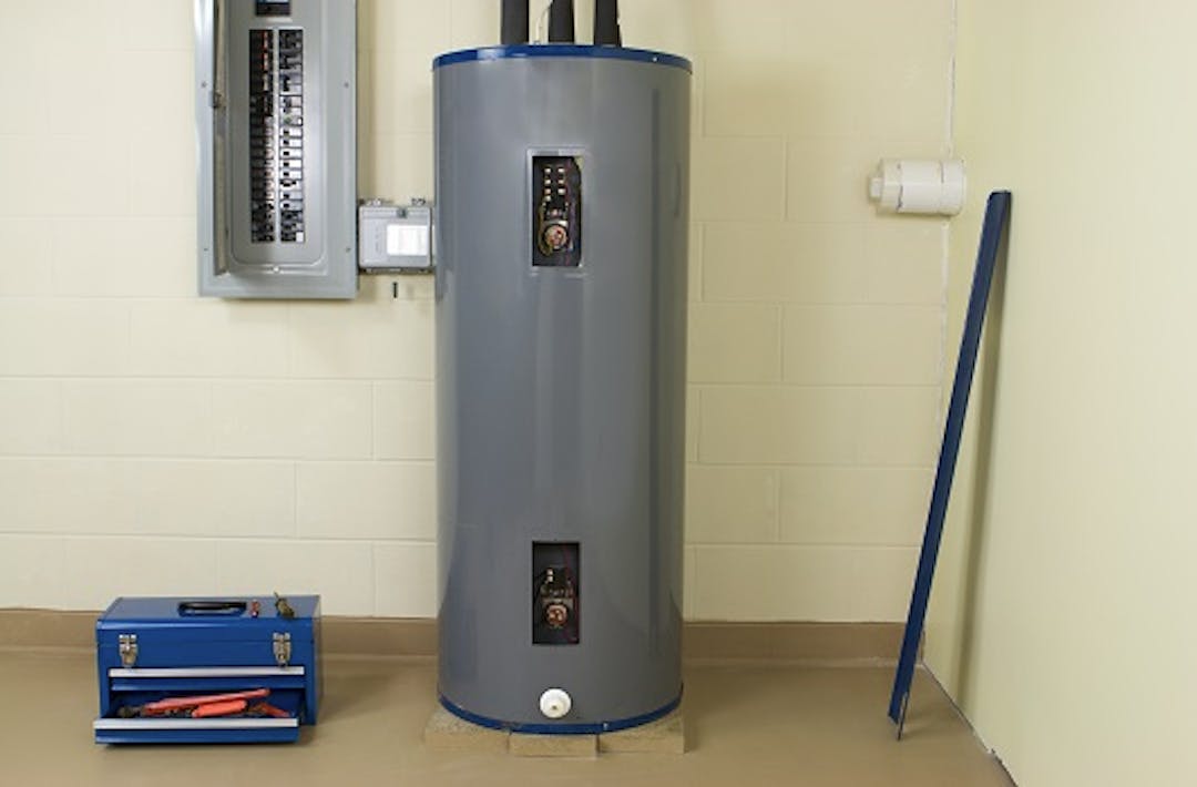 Mid-installation of electric hot water tank with blue tool box on the floor and electrical panel on the wall