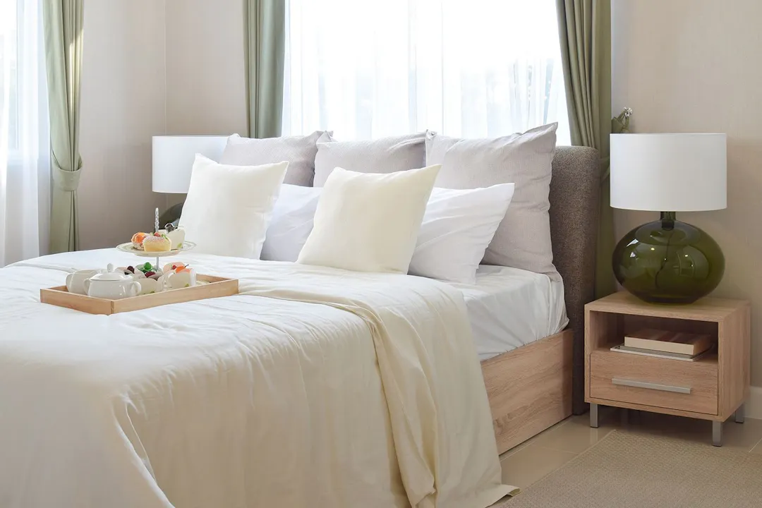 A bedroom with bright light streaming through a window. A tray of breakfast items sits on a bed.