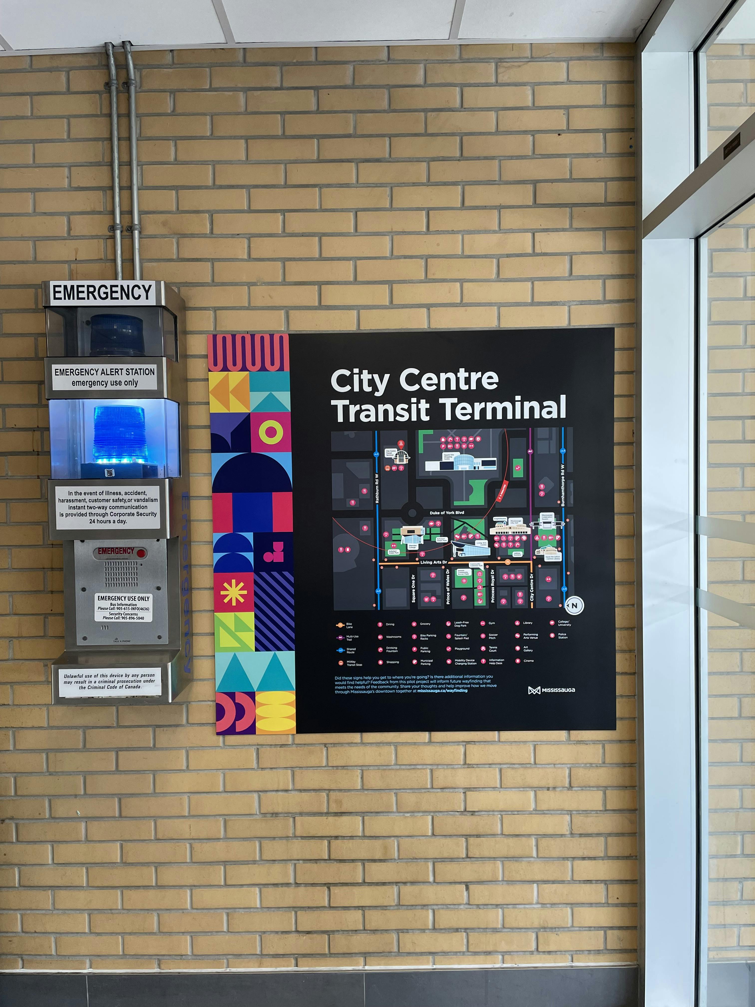 A map of the City Centre Transit Terminal displayed on a wall, next to an emergency alert station with a blue light.