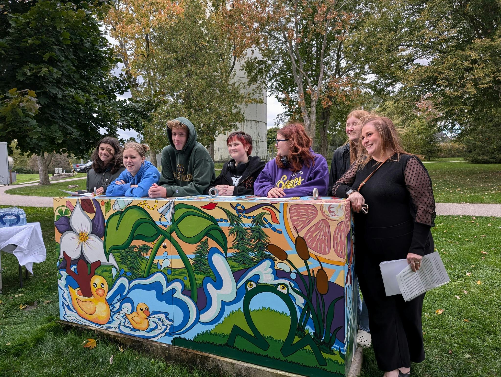 Students stand behind an electrical box that has been painted with a mural