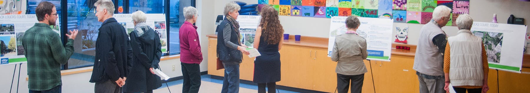A group of 10 seniors gathered in a classroom, reading information boards and talking to a couple presenters