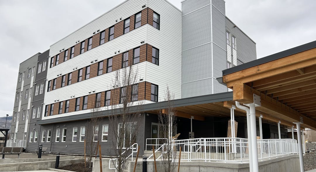 four-story building with grey, white and brown coloured exterior panels, large windows, and a covered entrance.