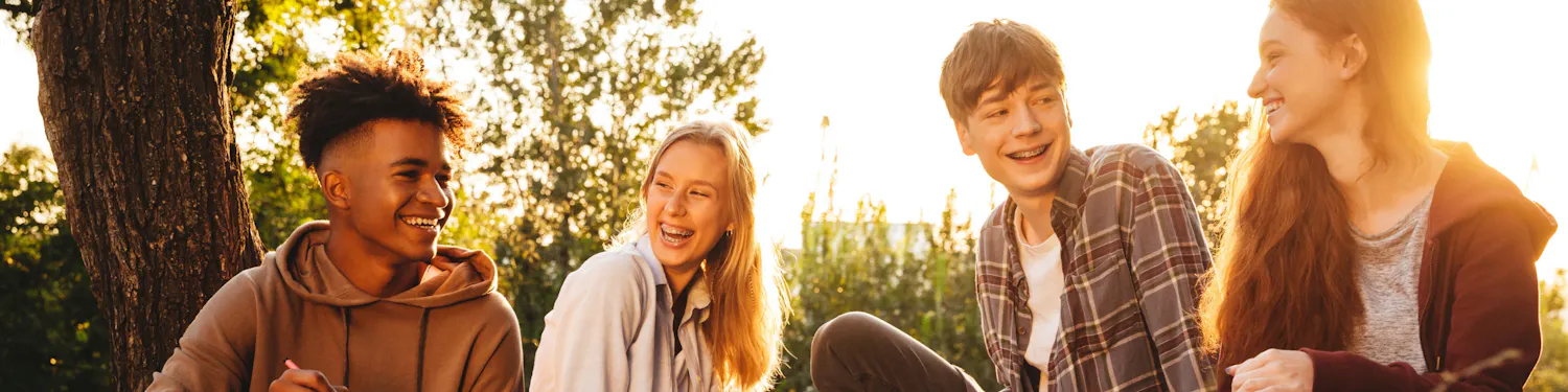 Four teens sitting in the grass smiling at each other while studying