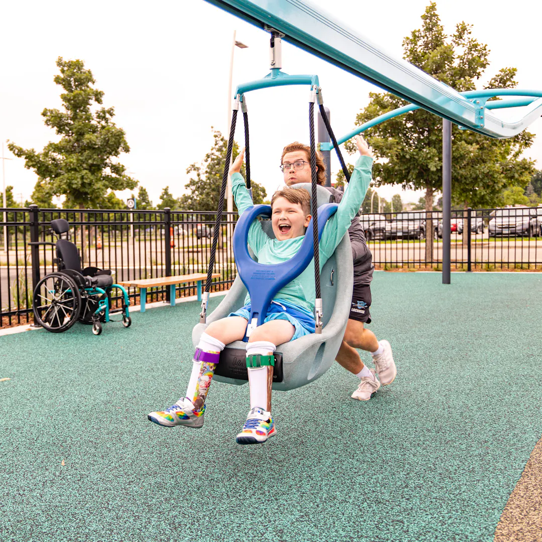 Person pushing happy child on accessible zipline