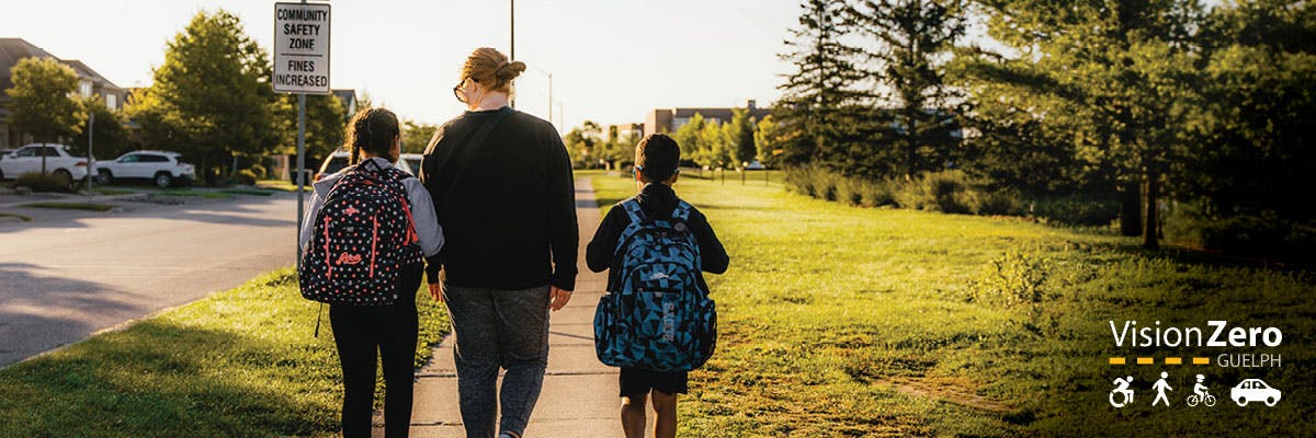 Two children with backpacks walk with an adult along a sidewalk. A sign stating "Community Safety Zone" is in the image. 