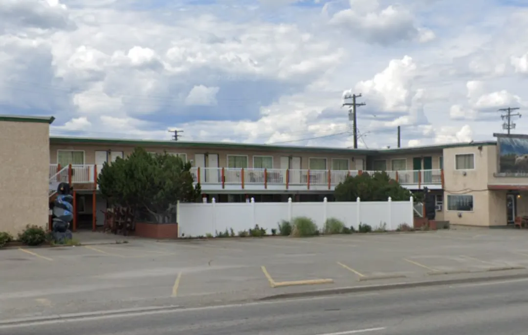 A parking lot outside a two-story motel with several vehicles parked, including a black Dodge Ram truck in the foreground.