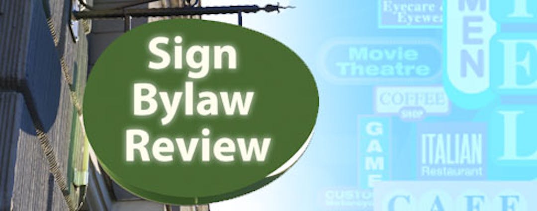 Picture of a building sign with the words "sign bylaw review"  printed on it