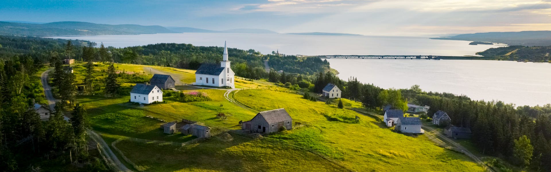 A landscape photo of the Highland Village in Iona, with the Bras d'Or Lake and hills in the background. 