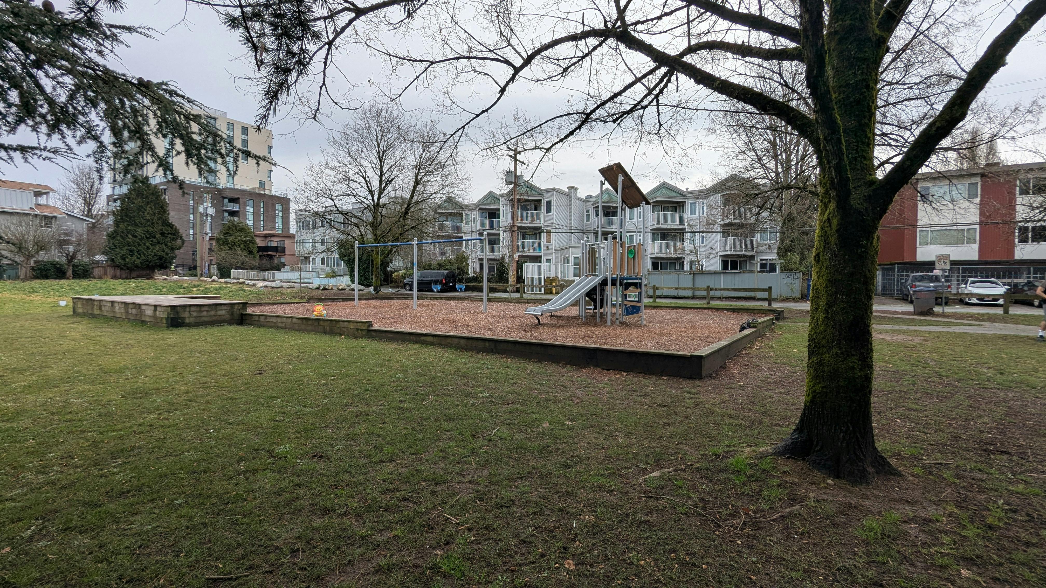 Image of playground with swing set and slide structure on wood chip surface.