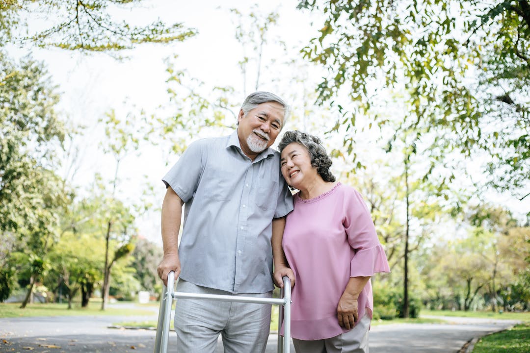 An older couple walking outdoors using a walker.