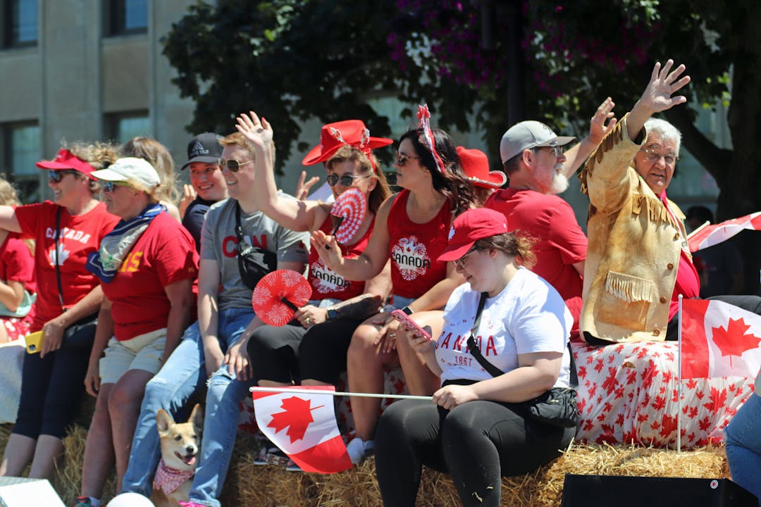 People on a float in a parade wearing red and white clothing with Canada flags