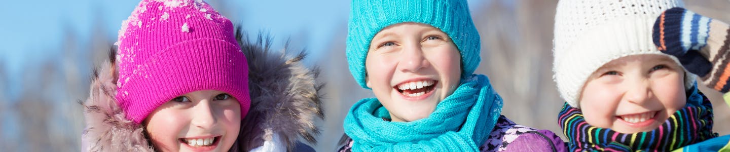 Three kids wearing toques and scarves smile at the camera
