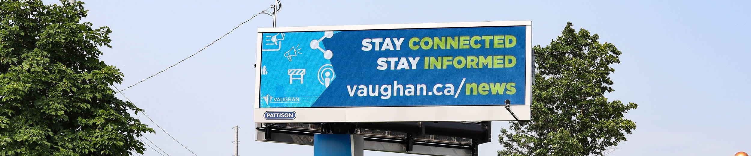A blue sky with trees in the background and a digital billboard in the foreground with the words Stay Connected Stay Informed