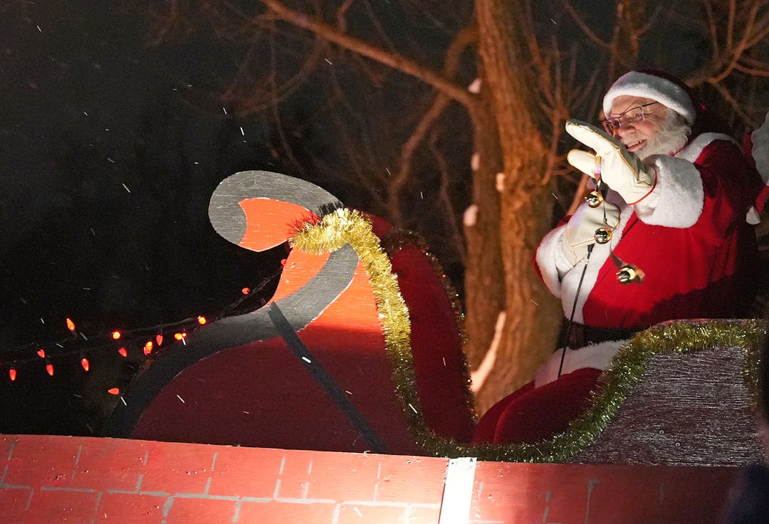 Santa Claus waves to the crowd from a wooden sleigh.