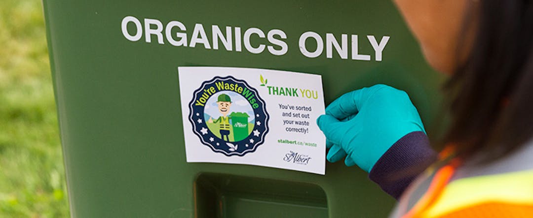 City staff member places a "Thank You" sticker on a Green Organics Cart that has been correctly sorted