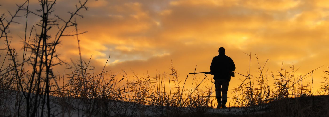 Silhouette of  hunter with gun walking in the sunrise