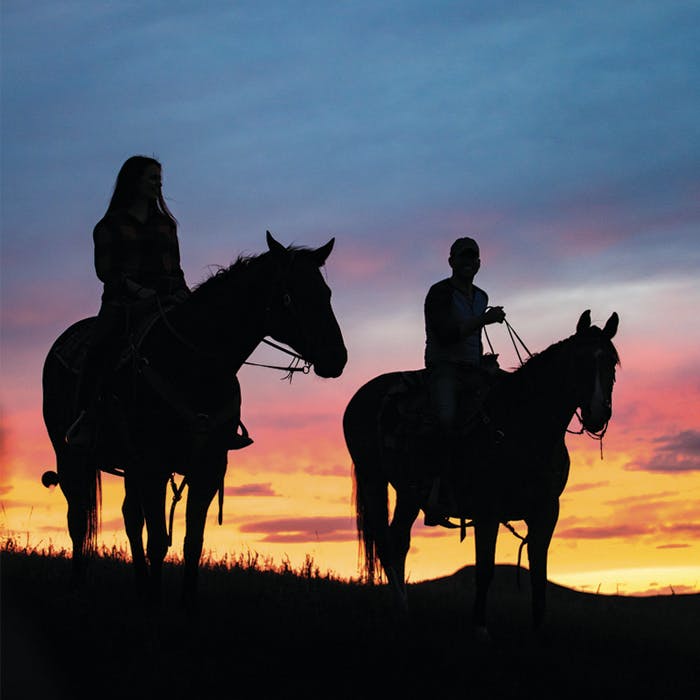 Silhouettes de deux personnes à cheval au coucher du soleil