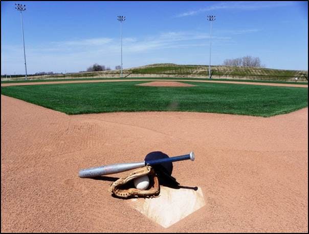 Image of a baseball bat, glove with ball and a hat on homeplate looking out on the Premier Baseball Diamond.