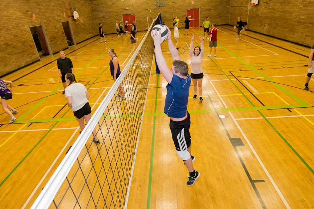 Inside a gym, young adults are playing volleyball