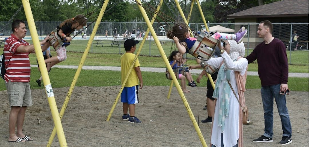 Adults push children on swings on the existing playground at Kiwanis Park.