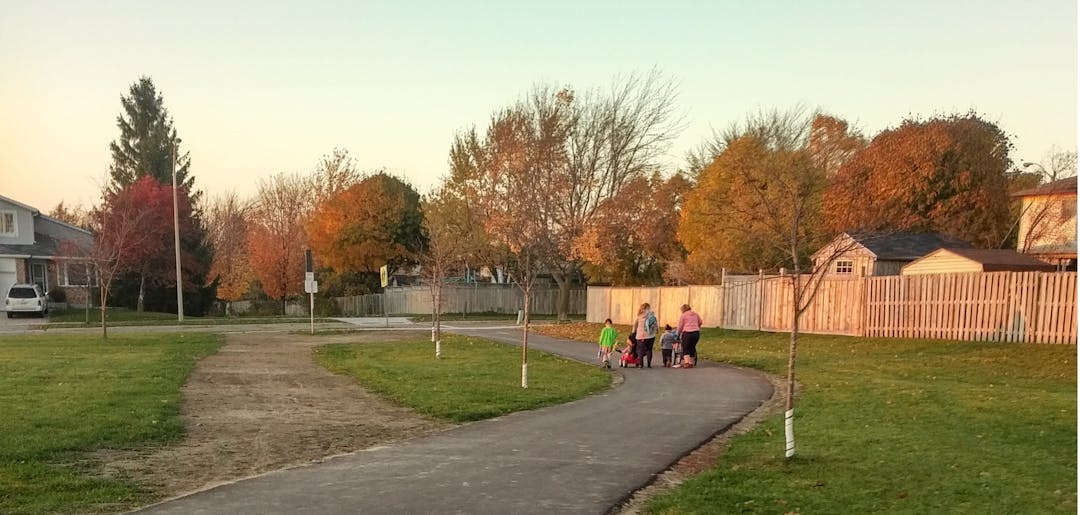 Children and adults walk up a paved trail running next to the old dirt path that leads away from the school.