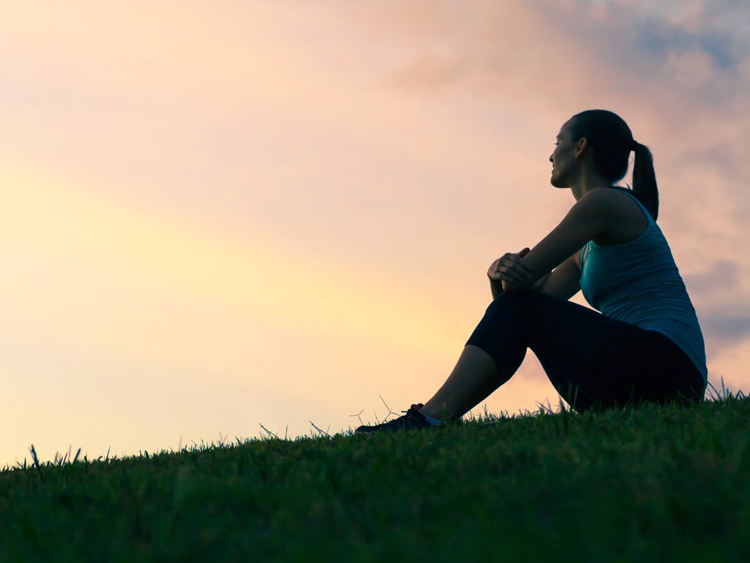 Woman sitting on a hill at sunset Woman sitting on a grassy hill at sunset.