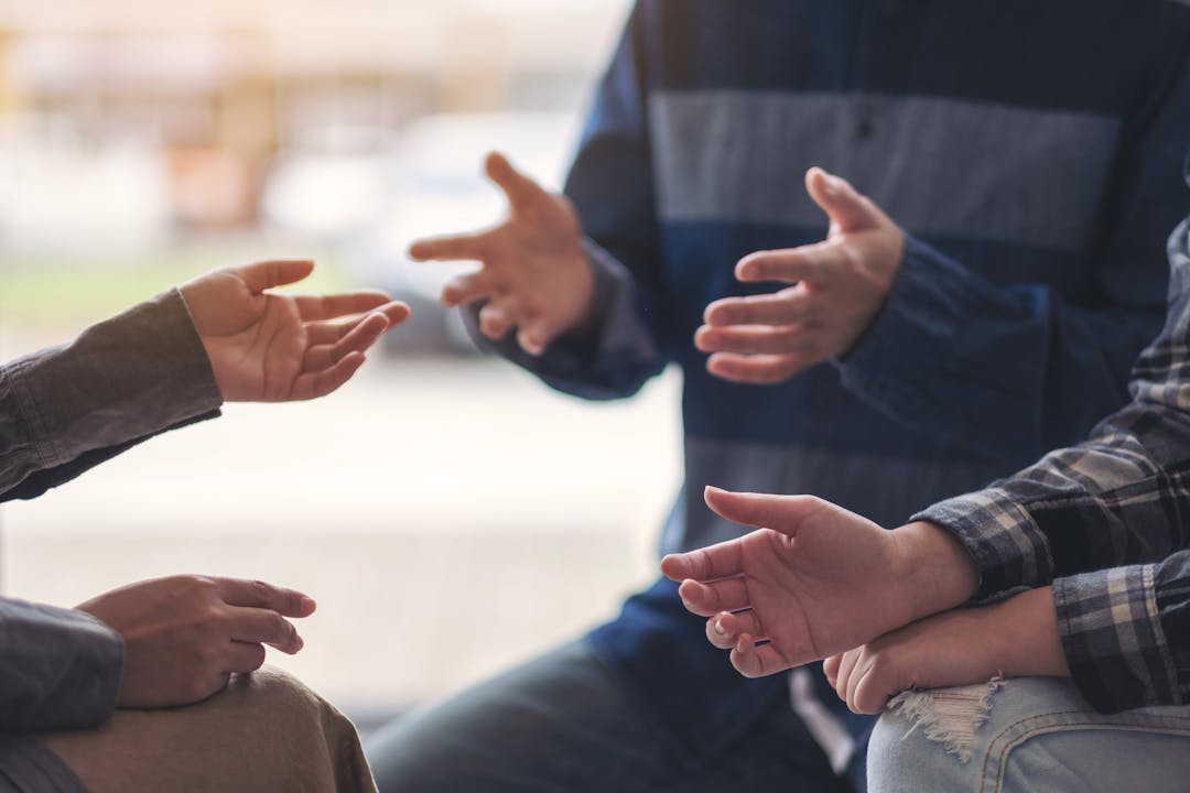 Close up of hands of a group leaning in close together in a circle engaged in conversation.