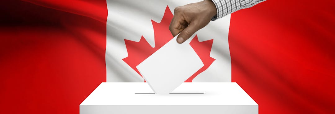 Hand submitting a paper ballot in front of a Canadian flag