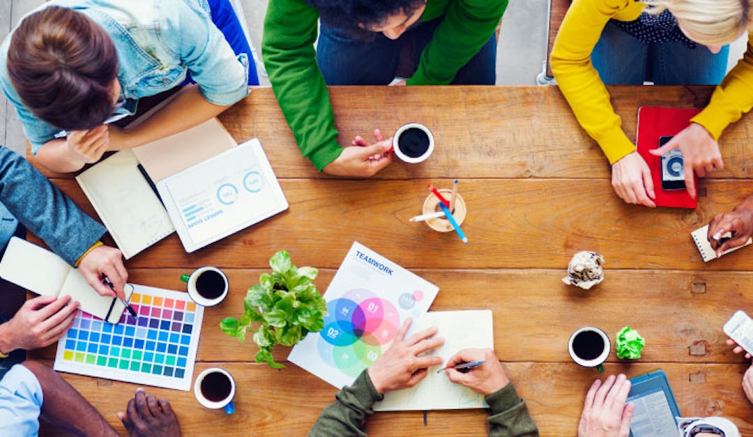 People sitting at a table, working on a project together with charts, graphs and coffee