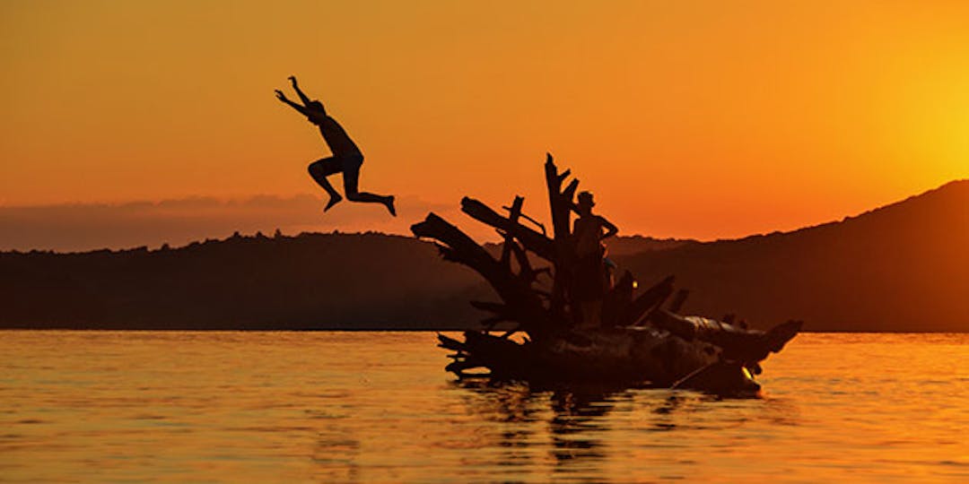 sunset photo of person jumping into the water