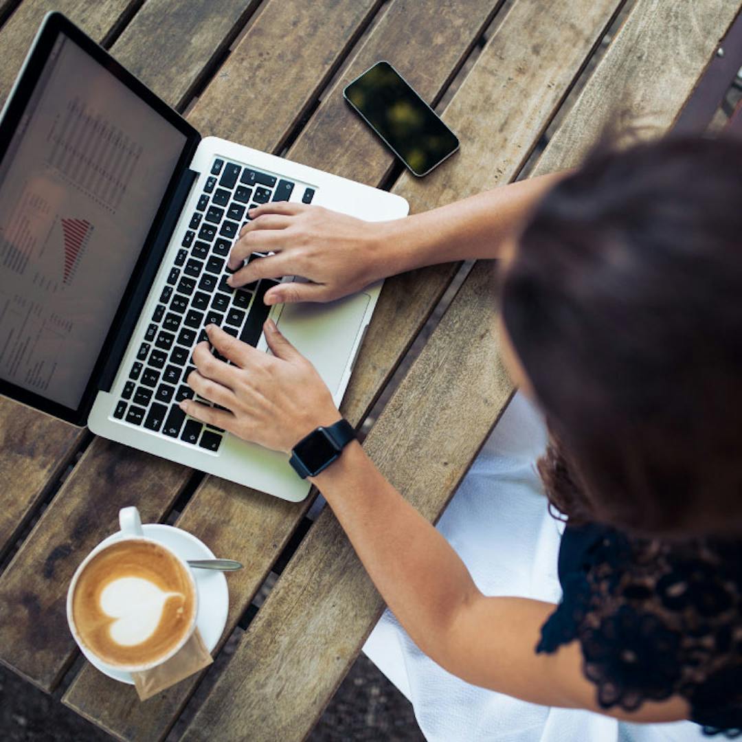 Woman typing on a laptop having a coffee.